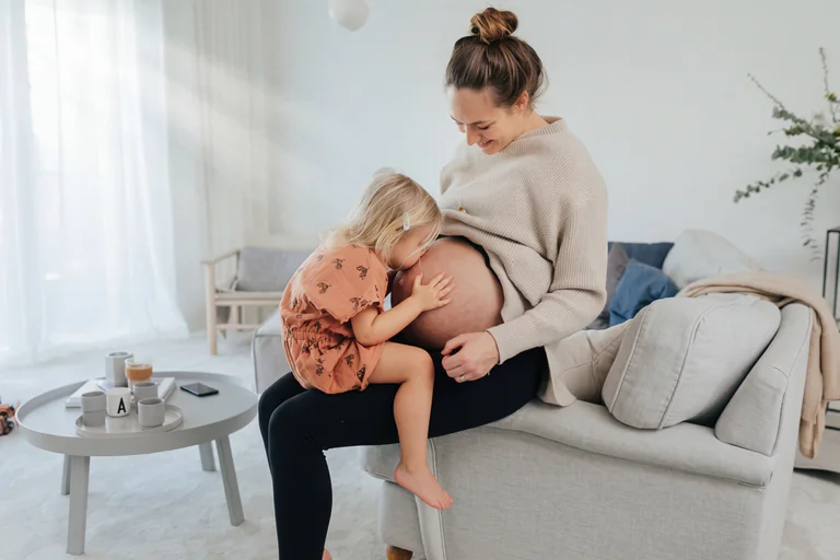 Gravid kvinna med dotter som kysser hennes mage.