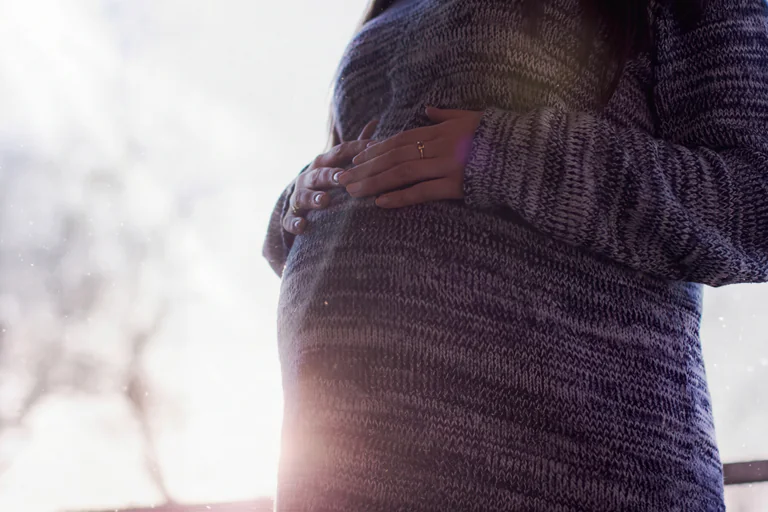 En gravid kvinna håller händerna över sin mage inomhus.
