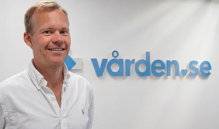 En man står framför en vägg med Vården.se logotyp.