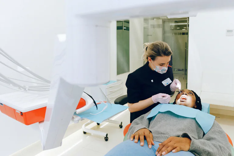Tandläkare med instrument undersöker en patient i munnen, sittande i en tandläkarstol.