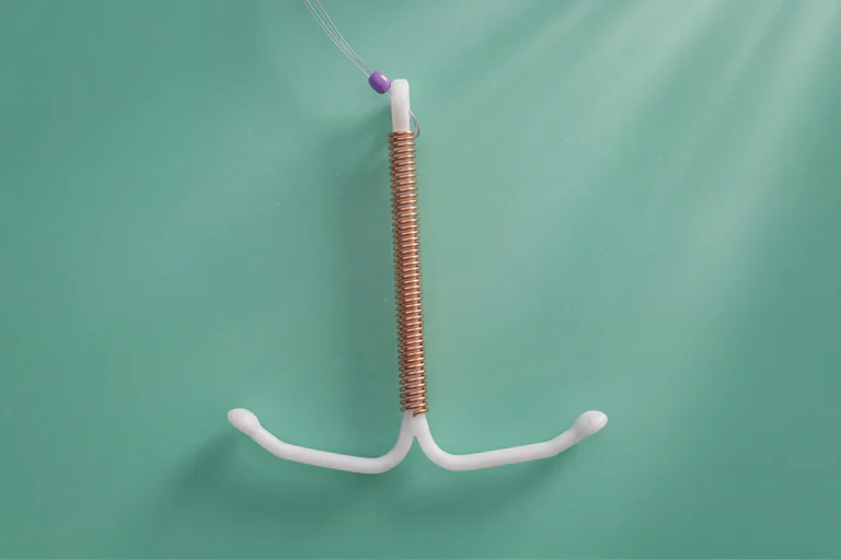 Ett intrauterint preventivmedel (IUD) i form av ett T-format plastinstrument med en spiral av koppartråd lindad runt en stomme, med tunna trådar hängande ner från toppen, på en turkos bakgrund.