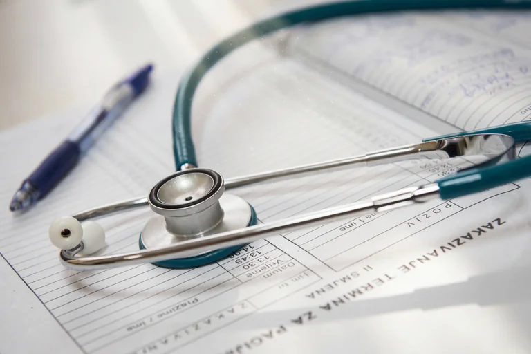 Ett stetoskop och en penna ligger på ett patientformulär med tidbokningsscheman.