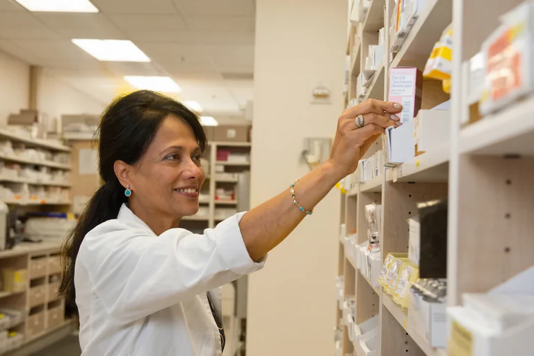 Farmaceut i vit rock tar en låda med medicin från en hylla på apoteket.