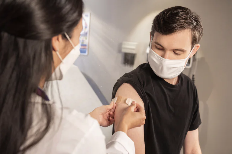 Sjukvårdspersonal applicerar ett plåster på en mans arm.