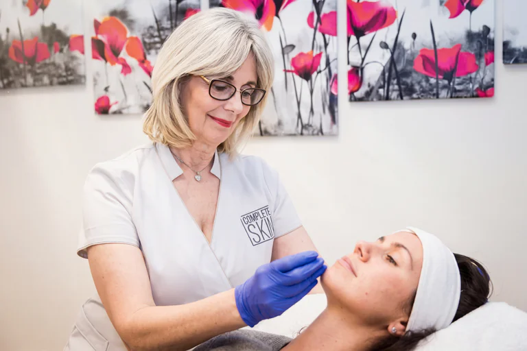 En professionell person med blå handskar utför en hudbehandling på en patient som ligger på en brits.