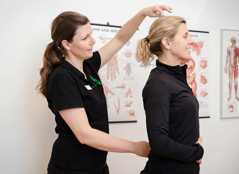 En fysioterapeut undersöker en kvinnlig patients hållning i ett undersökningsrum.