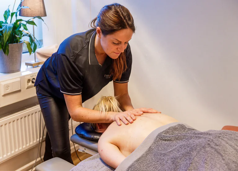 En fysioterapeut masserar en patients rygg på en massagebänk i ett behandlingsrum.