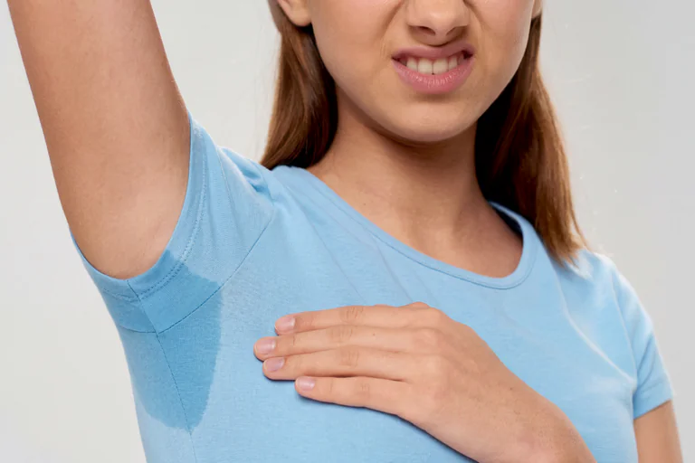 En kvinna som ser obekväm ut och håller upp sin arm och visar upp en svettfläck på sin ljusblåa t-shirt.
