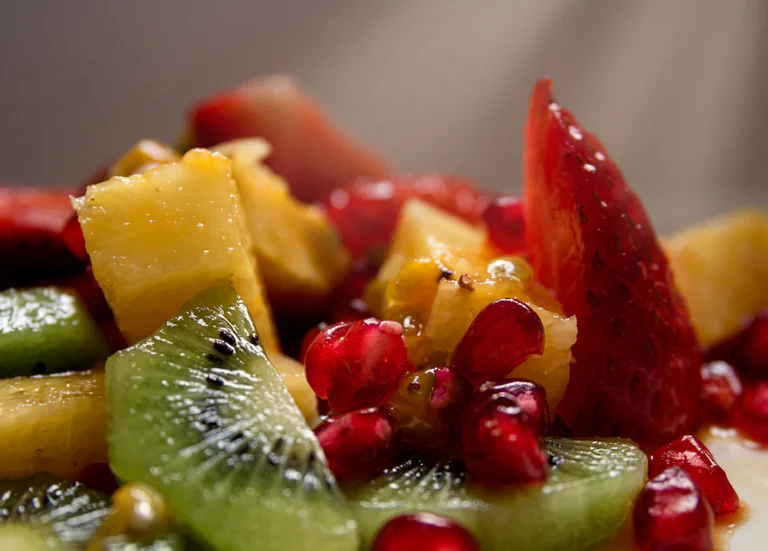 Närbild på en fruktsallad med kiwi, jordgubbar, ananas och granatäppelkärnor.