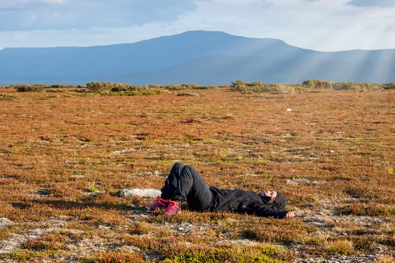 Person ligger avslappnat på gräsmark med berg i bakgrunden.