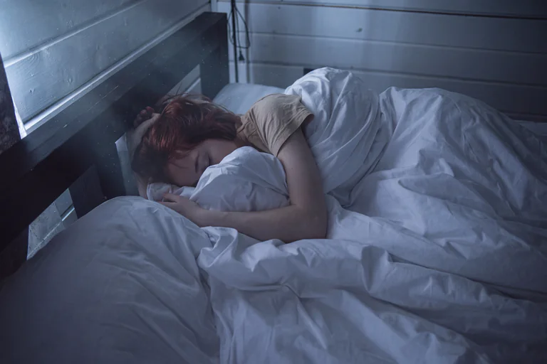 Person som sover i en säng täckt av ett vitt täcke.
