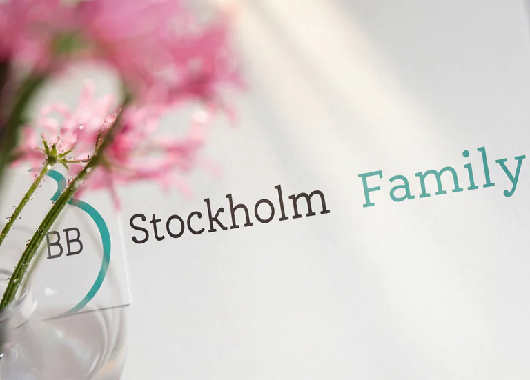 En illustration med texten "Stockholm Family" i svart och blågrön färg, med rosa blommor i bakgrunden.