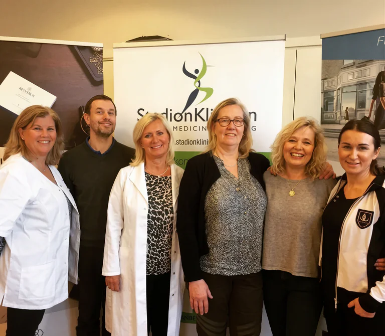 En grupp på sex vårdpersonal poserar framför en banderoll.