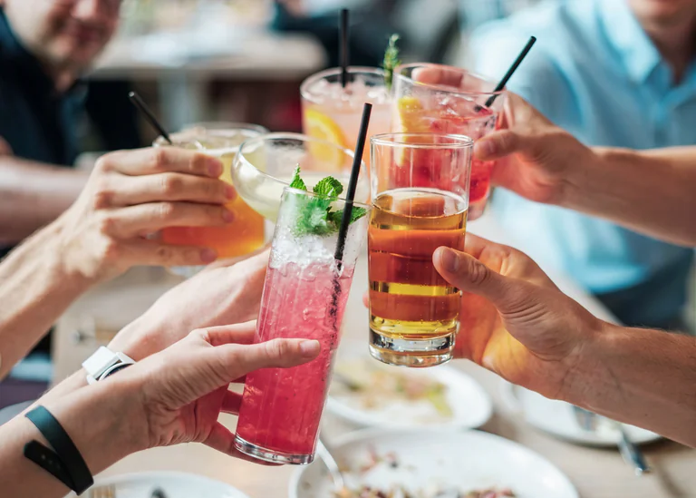 En grupp människor skålar med färgglada drinkar runt ett bord på en restaurang.