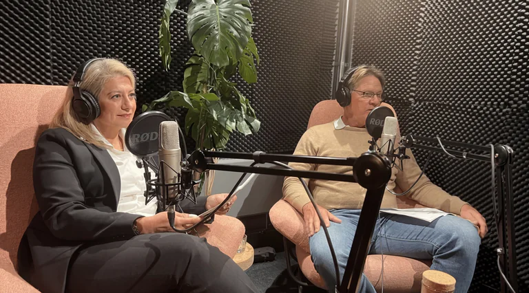 Två personer sitter i hörlurar med mikrofoner framför sig i en ljudisolerad studio.