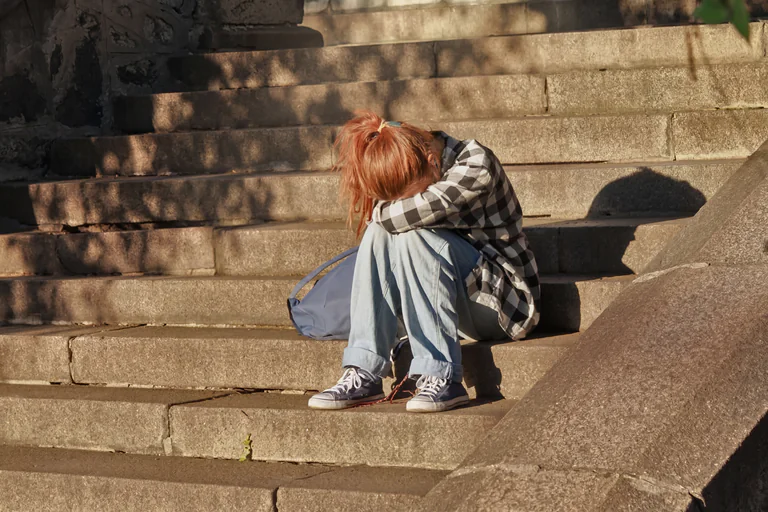 En person sitter hopsjunken på en stenlagd trappa och gömmer ansiktet i händerna.