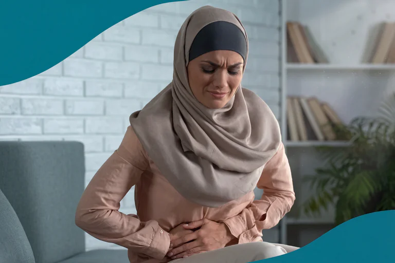 En kvinna i hijab håller sig om magen med smärta i ett klinikrum.