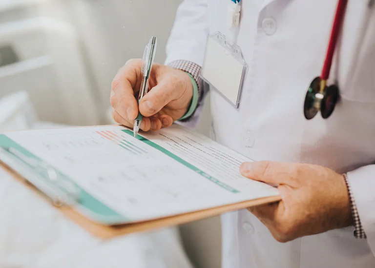 Läkare i vit rock skriver på ett patientformulär med en penna.