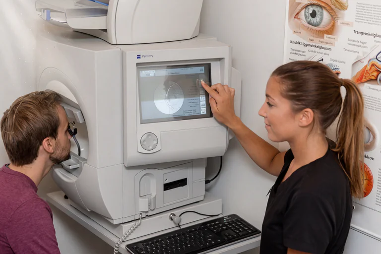 En optometrist som interagerar med en ögonundersökningsmaskin medan en patient undersöks.