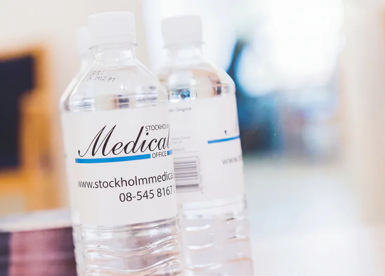 Två märkta flaskor med vatten från Stockholm Medical Office som står på ett bord.
