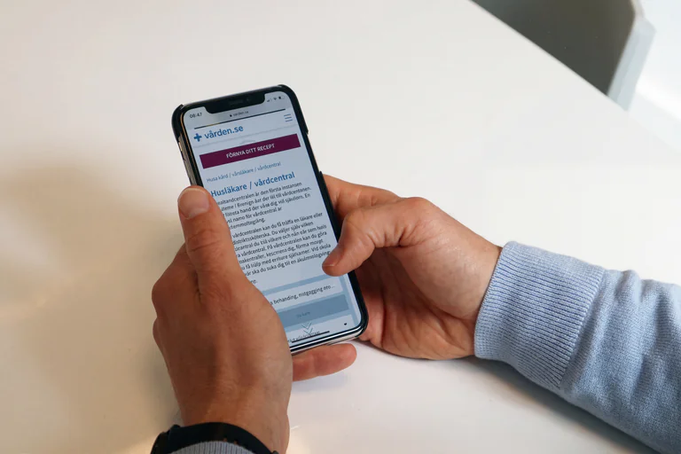 Person som håller i en smartphone och navigerar på en svensk vårdapp.
