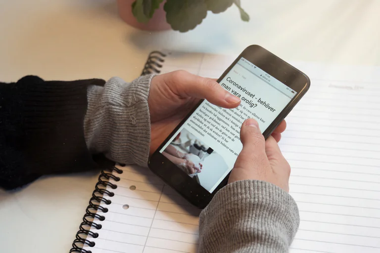 En person håller en smartphone och läser en artikel om coronaviruset.